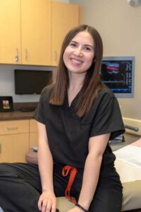 Smiling female team member – Alpine Surgical professional seated in exam room near equipment