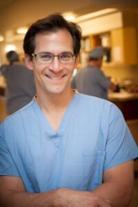 Board-certified oral surgeon – Male Alpine Surgical professional in blue scrubs smiling confidently