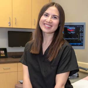 Female team member in scrubs – Smiling staff member seated near diagnostic equipment