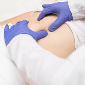 Abdominal exam – Gloved doctor’s hands palpating patient’s stomach