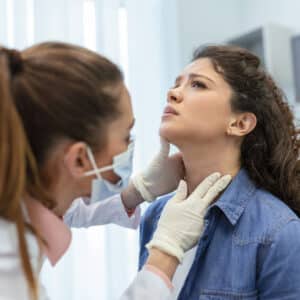 ENT examination – Female patient having throat examined by doctor with tongue depressor