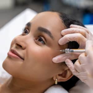Facial skin checkup – Doctor examining woman’s face with gloved hand and medical light