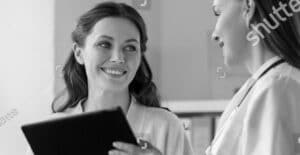 Female medical professional – Smiling woman holding clipboard in clinical setting