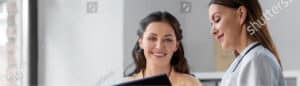 Friendly medical receptionist – Woman holding clipboard and smiling at Alpine Surgical front desk