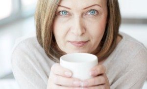 Mature woman holding a white mug and smiling, symbolizing recovery and patient comfort